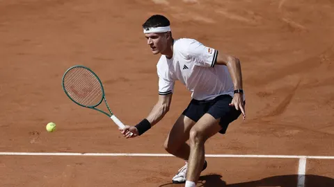 Tenisač Jakub Menšik u bijeloj majici udara lopticu na glinenom terenu