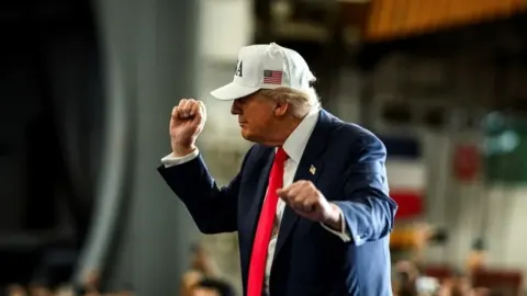 Donald Trump u tamnom odijelu s bijelom kapom i podignutim šakama.