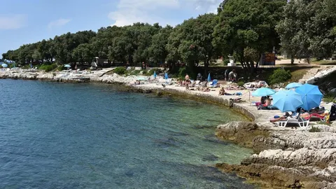 Kamenita obala Jadrana s kupalicima i plavim suncobrima