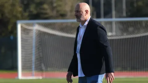 Trener Miodrag Božović stoji na nogometnom terenu ispred gola.