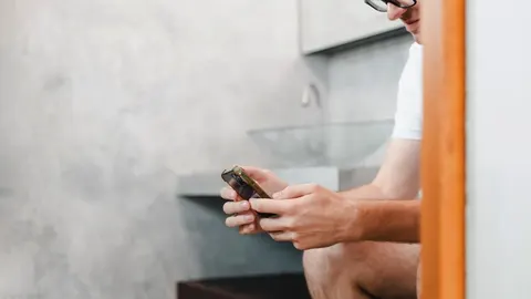 Muškarac u kupaonici sjedi i koristi pametni telefon