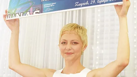 Žena s kratkom plavom kosom drži veliki novčani ček iznad glave
