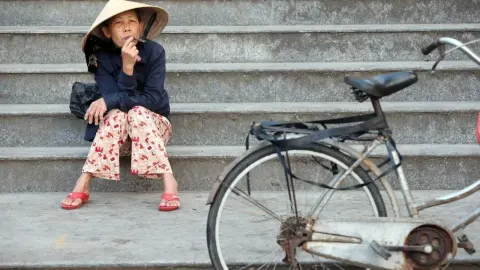 Starija žena s tradicionalnim šeširom sjedi na stubištu pored bicikla