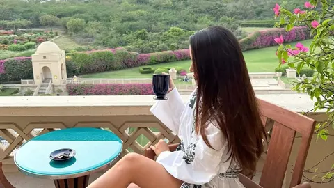 Žena s dugim smeđim kosom u bijelom odjeći pije iz crne šalice na terasi