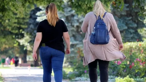 Dvije žene s viškom kilograma šetaju parkom odostrano od kamere