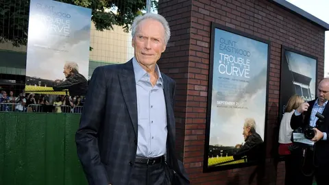 Clint Eastwood u tamnom odelu ispred promotivnih plakata filma