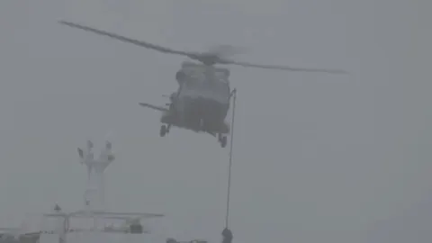 Vojni helikopter koji lebdi u zraku iznad broda po gustoj magli