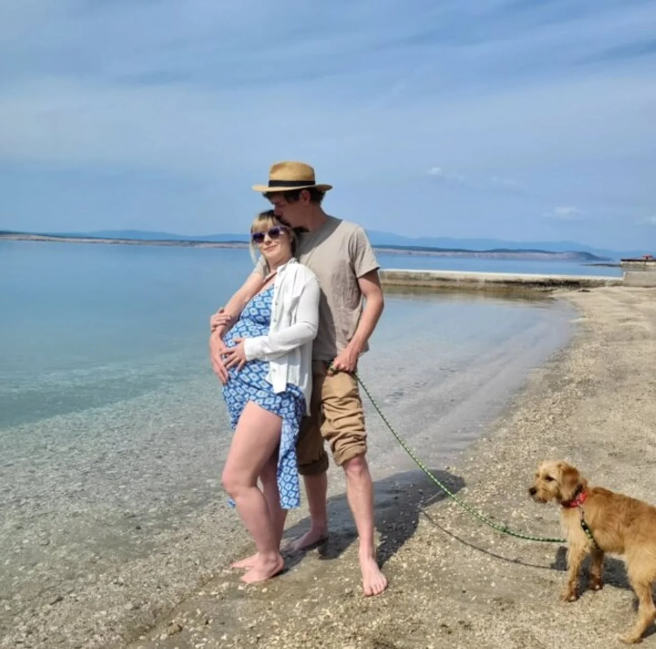 Trudna žena i muškarac s psom na kamenitoj plaži
