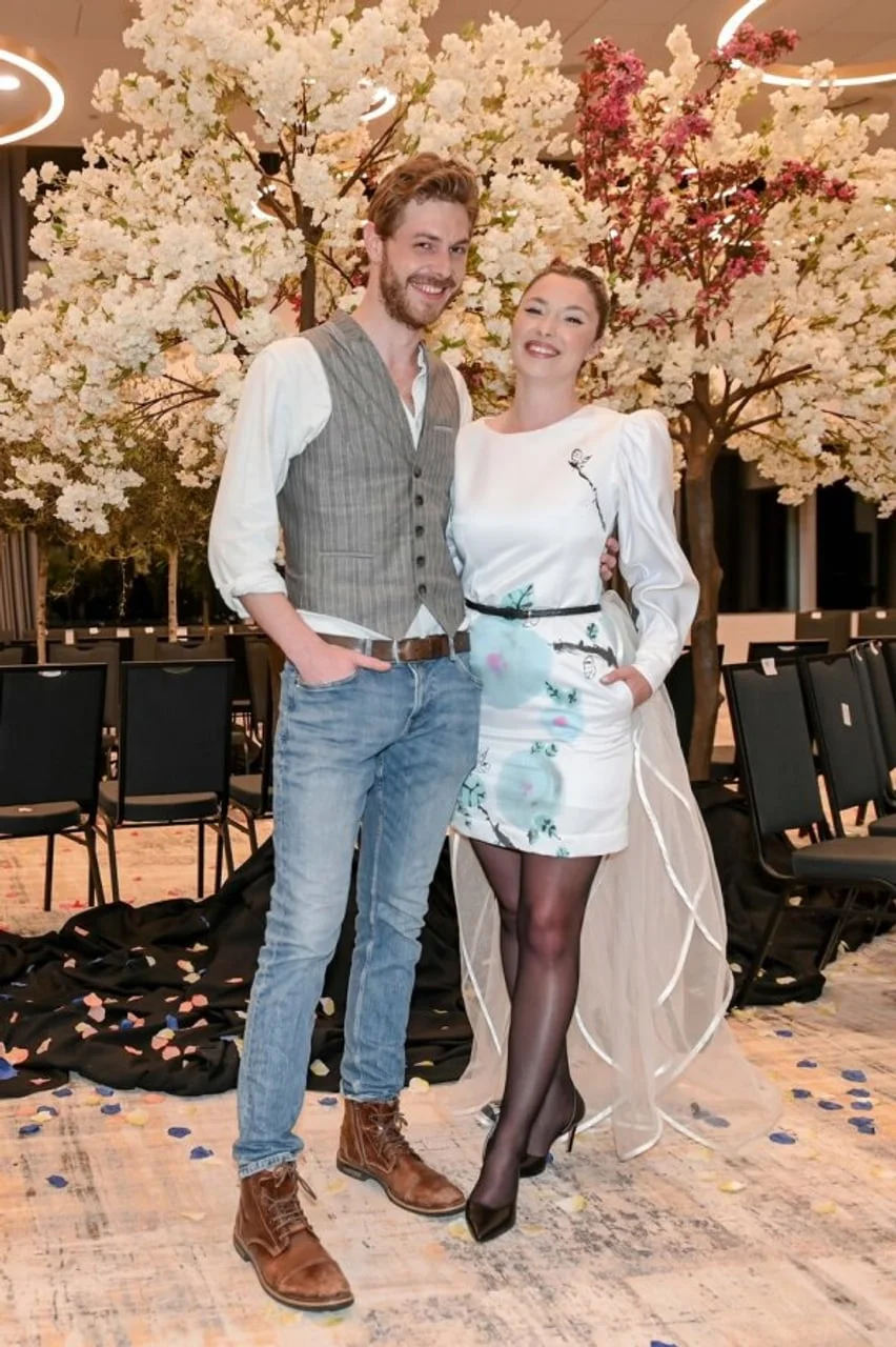 Par u elegantnoj odjeći ispred bijelih cvjetnih stabala