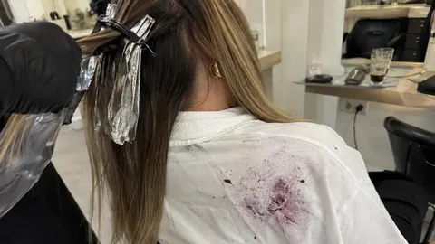 Ljubičasta mrlja od boje za kosu na bijeloj majici žene u frizerskom salonu