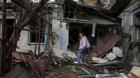 Uništena stambena zgrada s rušninama i žena u ružičastom prsluku