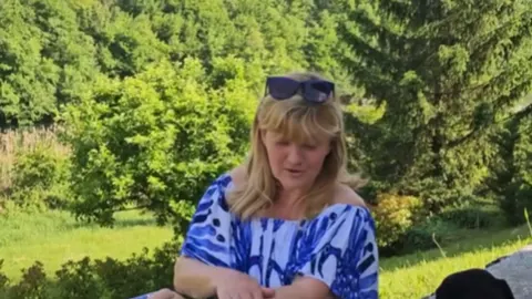 Sanja Doležal u plavoj haljini u prirodi pred zelenim drvećem