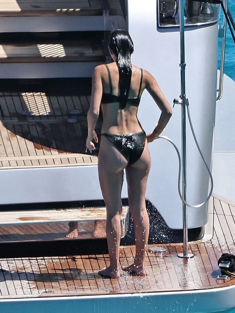 Full view of a woman in a black bikini standing on a yacht deck