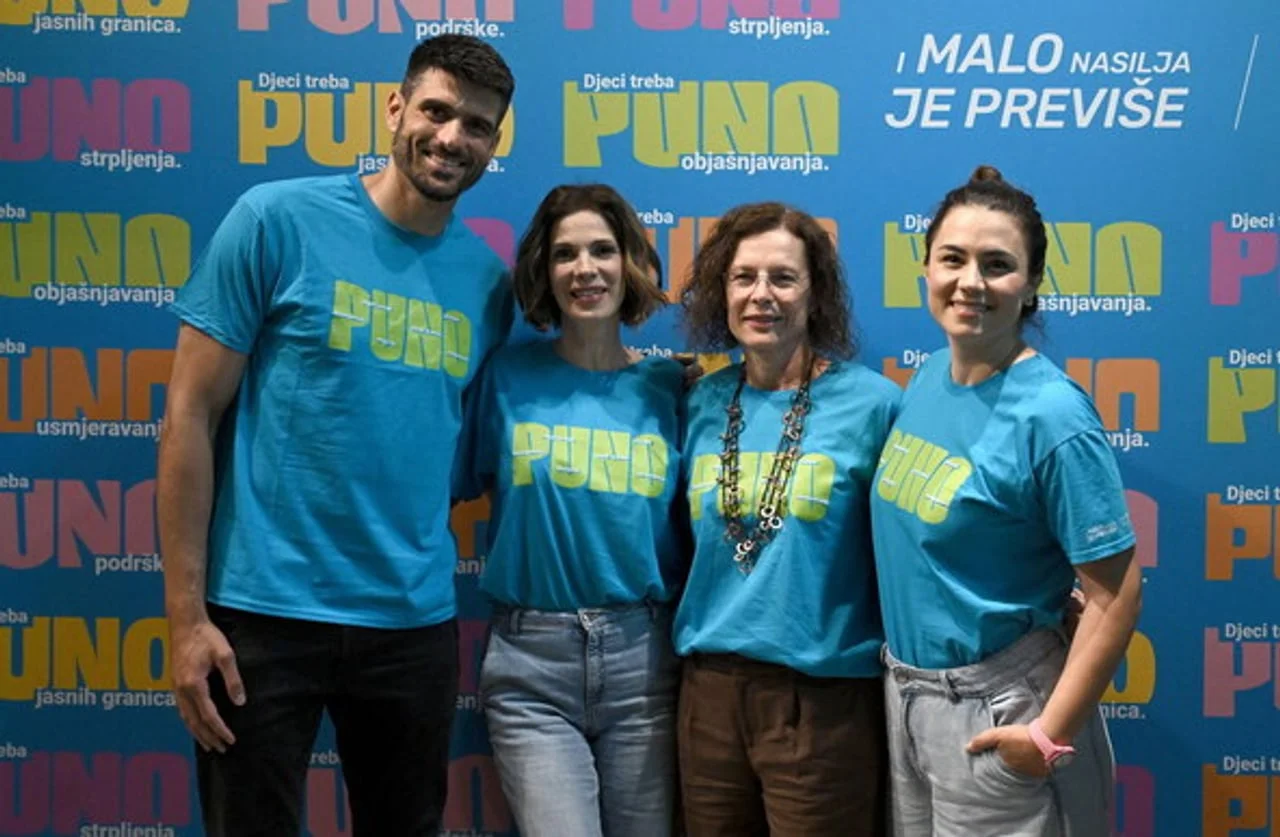 Grupa ljudi u plavim majicama ispred plavog zida s natpisima