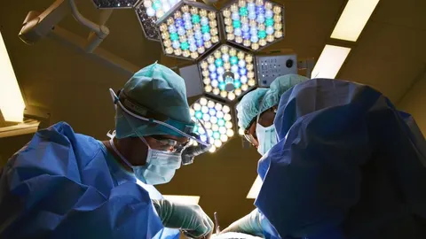 Kirurzi u sterilnoj odjeći i maskama rade pod operacijskim svjetlima