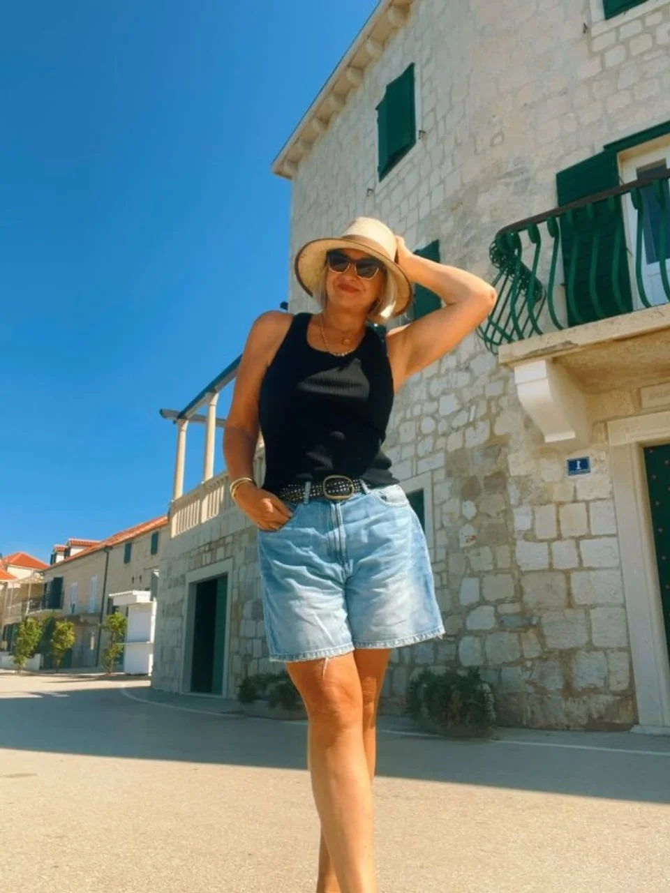 Žena u trapericama i crnom topu ispred kamene kuće
