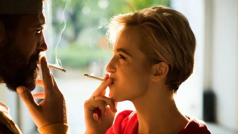 Muškarac i žena s cigaretama u ustima gledaju jedno u drugo