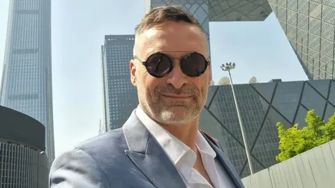 Ognjen Golubić u plavom odelu i sunčanim naočalama ispred modernih zgrada