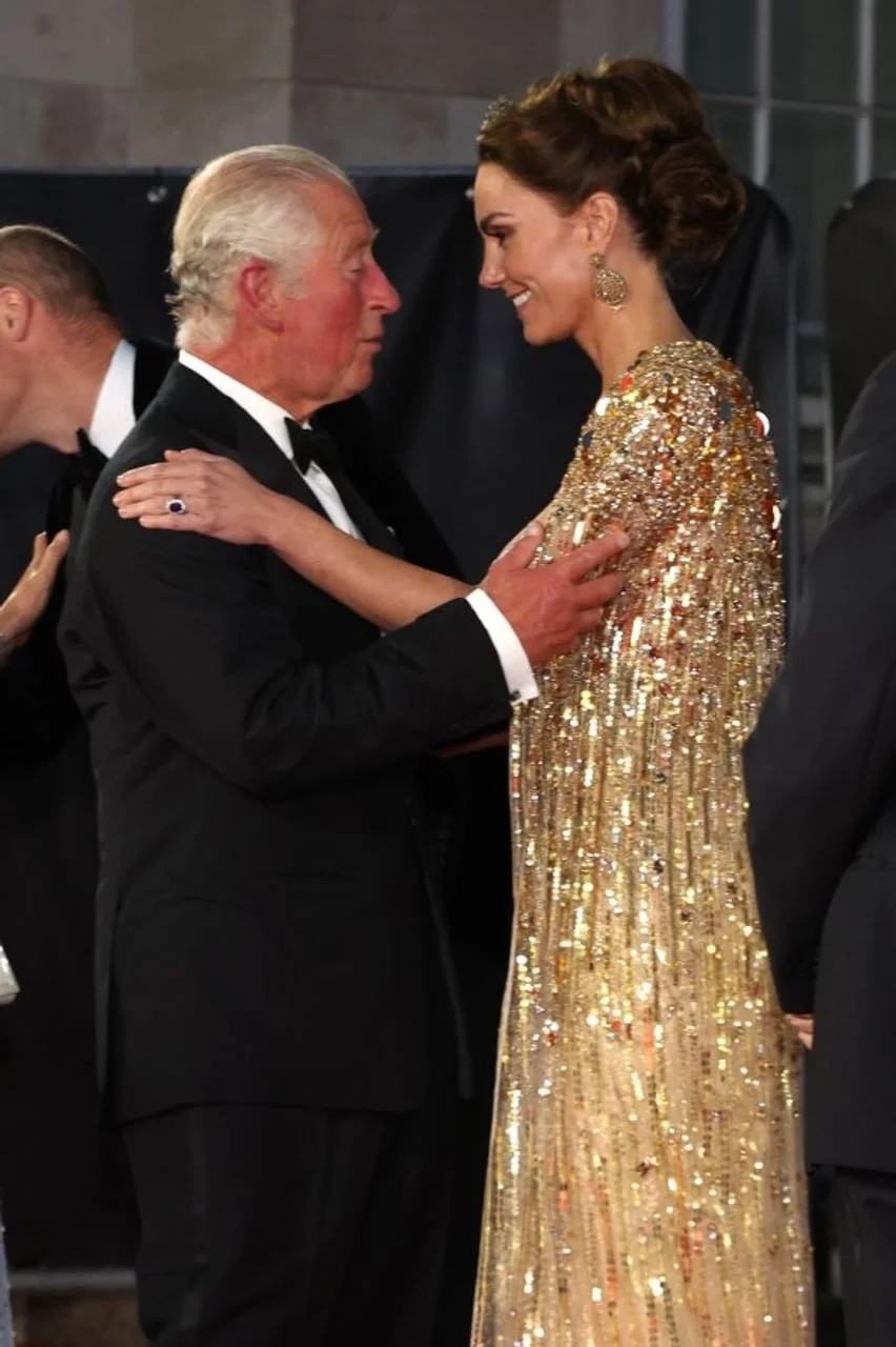 Kralj Charles i princeza Kate u zagrljaju, Kate nosi zlatnu šumirajuću haljinu