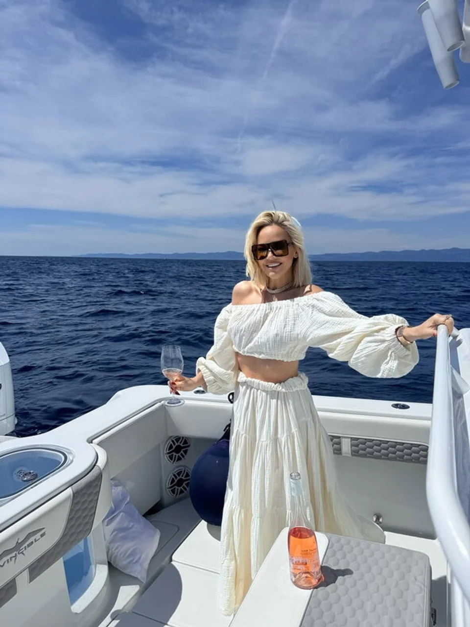 Žena u bijelom kompletu stoji na palubi bijelog glisera