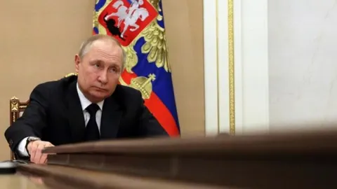 Vladimir Putin sjedi za stolom ispred ruske zastave