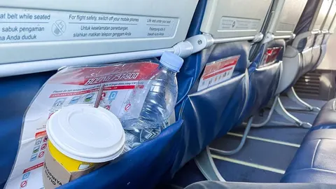 Plastična boca vode i čaša u džepu sjedala u zrakoplovu
