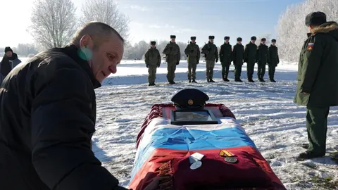 Muškarac tuguje pored lijesa prekrivenog zastavom na snježnom polju