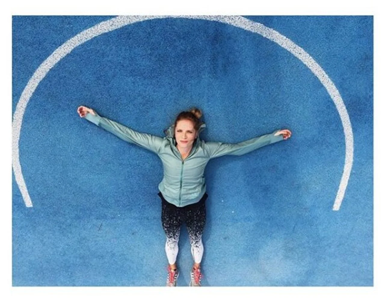 Žena u sportskoj odjeći leži raširenih ruku na plavom terenu