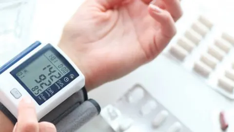 Digitalni aparat za tlak na zapešću ruke pored blister pakiranja lijekova
