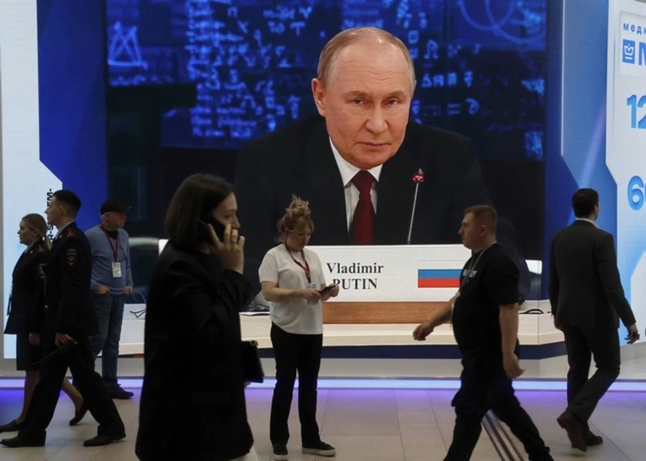 Veliki digitalni ekran s portretom Putina i ljudi koji prolaze ispred