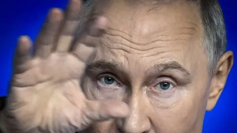 Krupni plan lica Vladimira Putina s podignutom rukom ispred lica