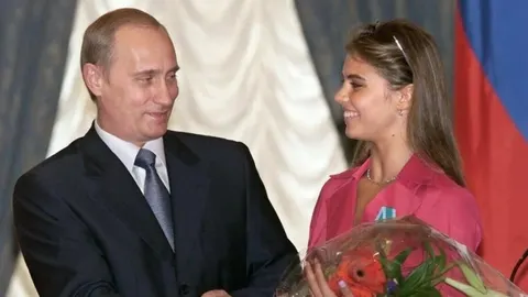 Vladimir Putin u odelu razgovara s mladom ženom koja drži buket cveća