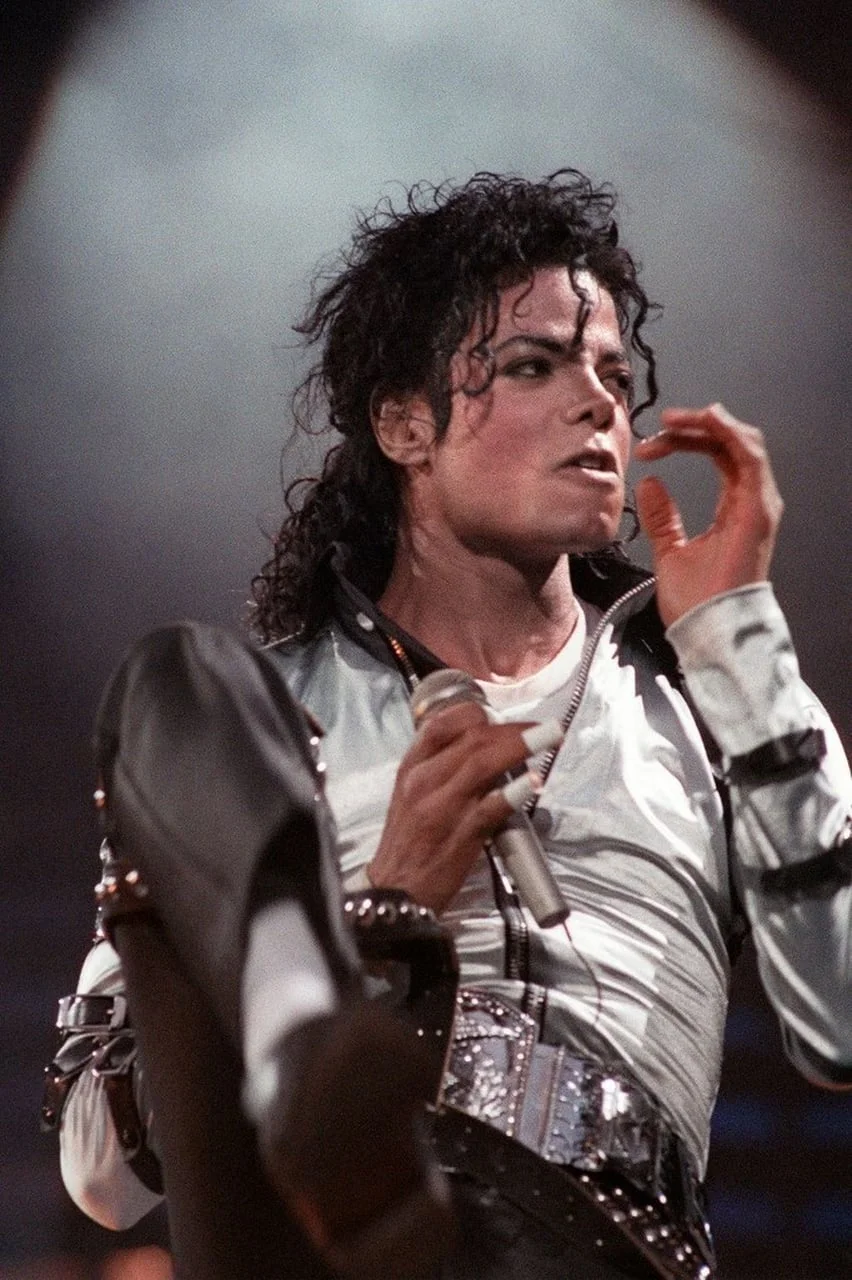 Michael Jackson s mikrofonom u bijeloj košulji i crnom remenu