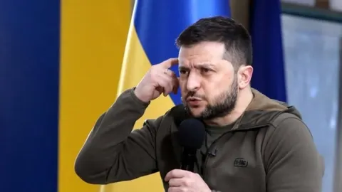 Ukrajinski predsjednik Volodimir Zelenski govori u mikrofon pred zastavom