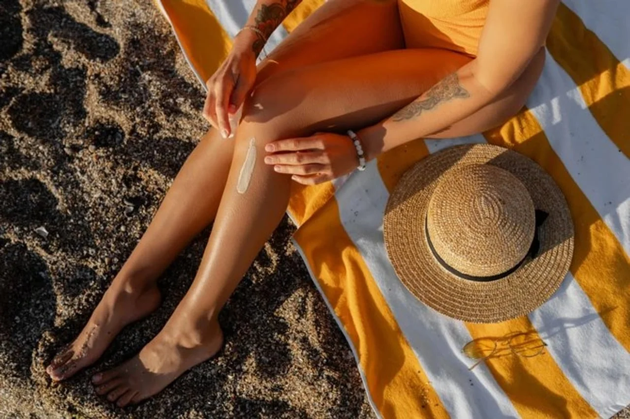 Krupni plan nogu žene koja nanosi kremu za sunčanje na plaži
