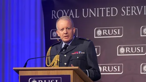 Britanski vojnik u uniformi govori za govornicom ispred RUSI pozadine