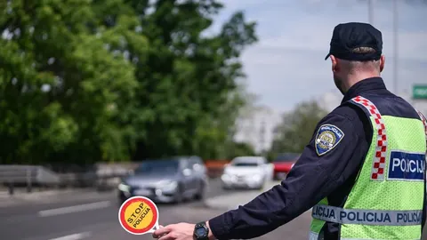 Policajac u fluorescentnom prsluku drži znak STOP POLICIJA na cesti