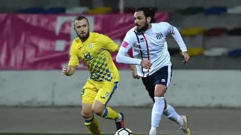 Dva nogometaša u žutom i bijelom dresu bore se za loptu na terenu