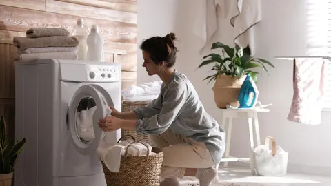 Žena vade bijeli rubilje iz perilice rublja u svijetloj prostoriji