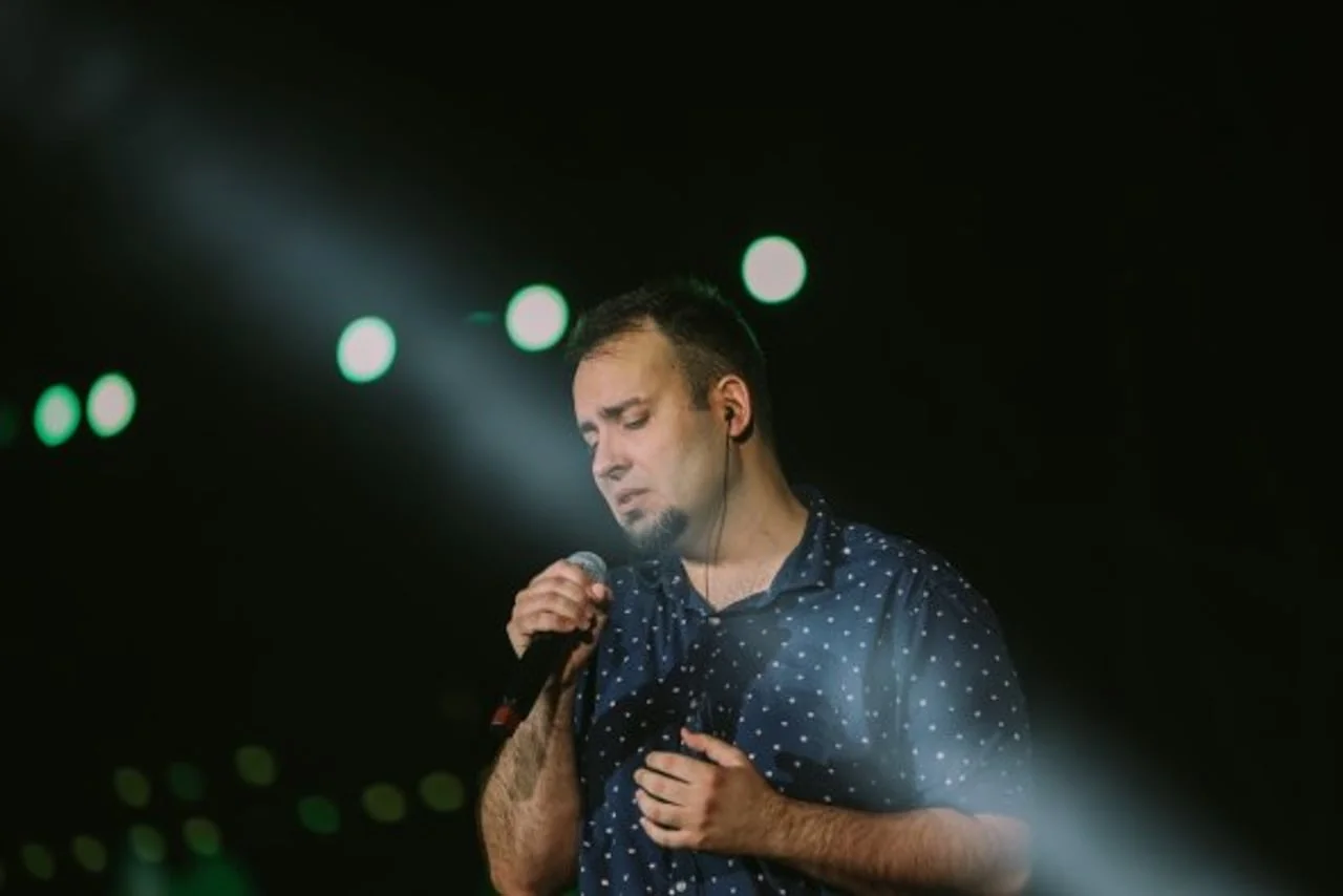 Muškarac u plavoj košulji s točkicama pjeva u mikrofon