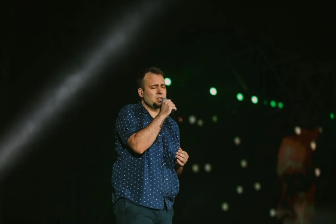 Muškarac u plavoj košulji pjeva zatvorenih očiju u mikrofon
