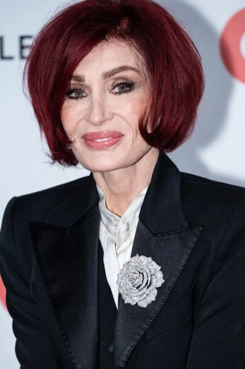 Portret Sharon Osbourne s crvenom kosom u crnom sakou s brošom
