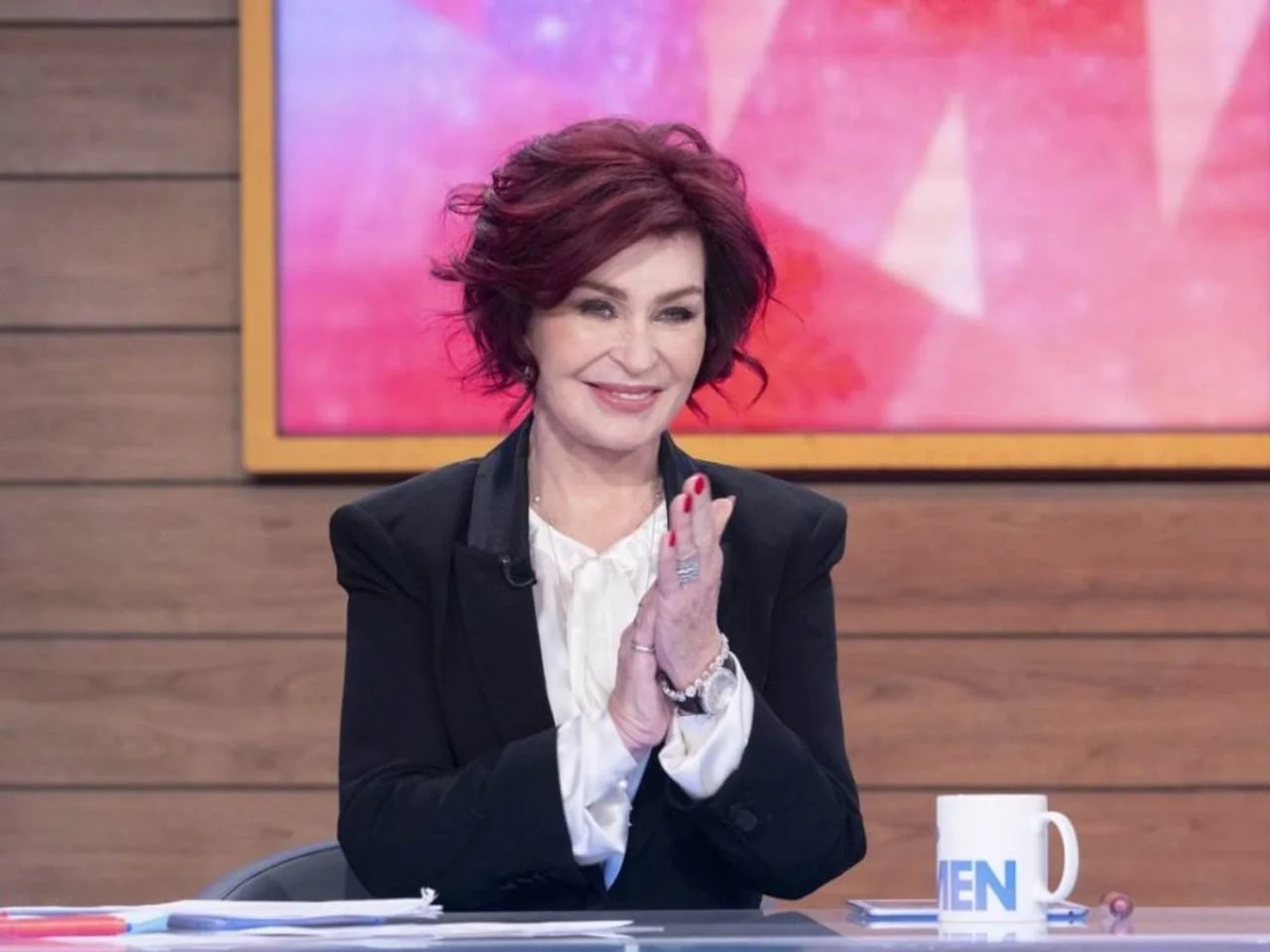Sharon Osbourne sjedi u studiju, pljeska rukama, crveni vobari