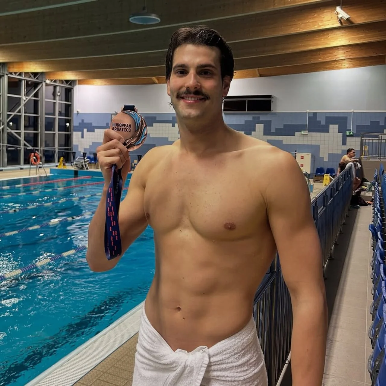 Plivač s medaljom oko vrata stoji pored olimpijskog bazena