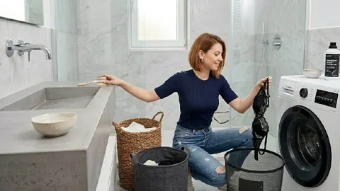 Žena u kupaonici drži crni komad odjeće pored perilice rublja