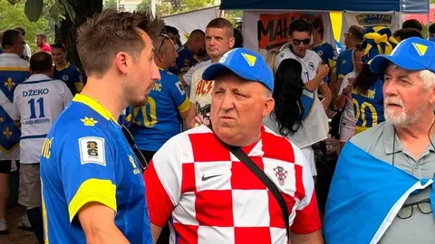 Muškarac u crveno-bijelom kockastom dresu okružen navijačima u plavim dresovima