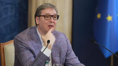 Aleksandar Vučić u plavom sakoju s naočalama, sjedi za stolom s mikrofonima