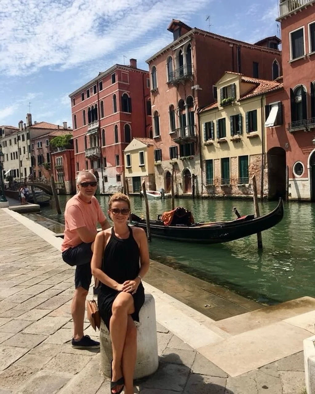 Par stoji pored kanala s gondolom i starim zgradama u Veneciji