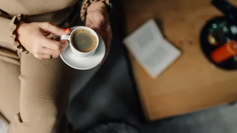 Krupni plan ruke osobe koja drži bijelu šalicu kave s pjenom
