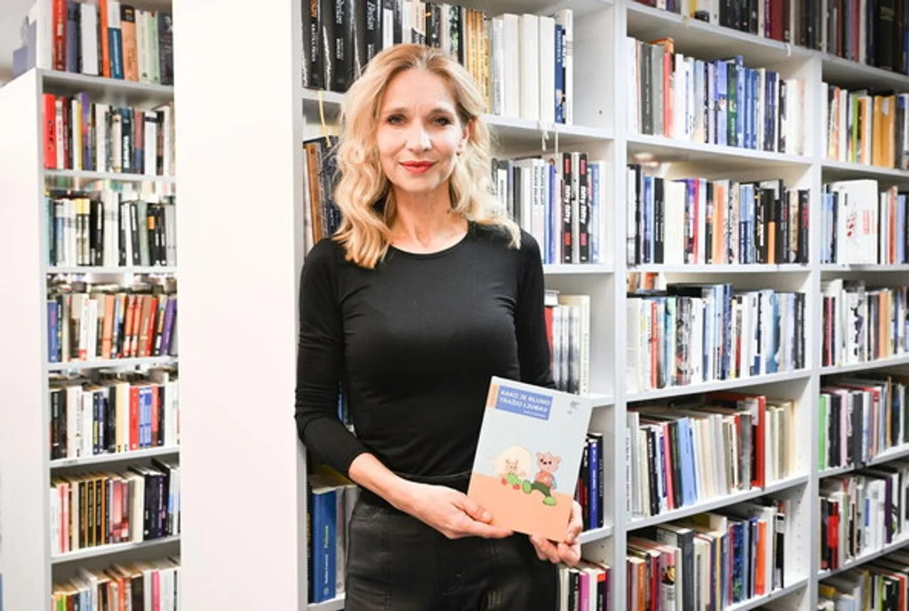 Žena drži knjigu stojeći ispred polica s knjigama u knjižnici